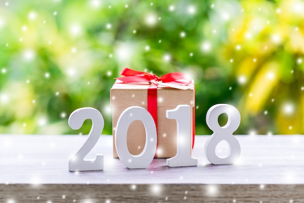 Hölzerne Zahlen, welche die Nr. 2018, für das neue Jahr mit Schnee und Geschenkbox auf hölzernem Tabellenhintergrund bilden.