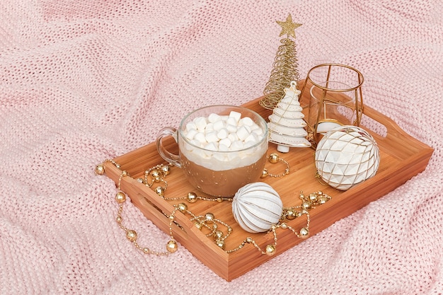 Hölzerner Behälter mit Schale Kakao, Eibischen und Weihnachtsdekorationen auf warmem gestricktem rosa Plaid.