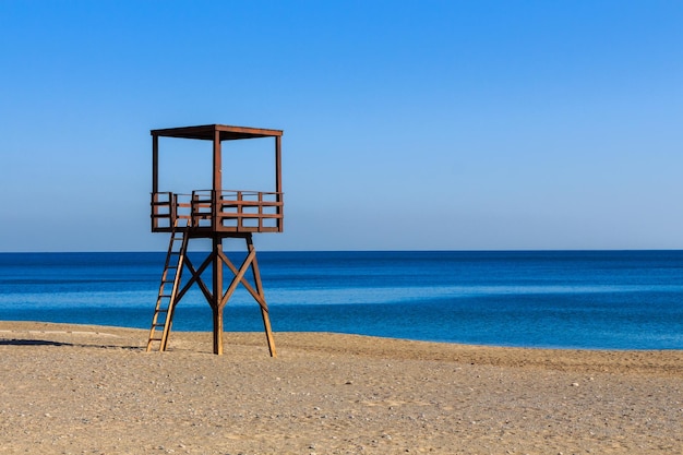 Hölzerner brauner Wachturm der Küstenwache am Strand mit blauem Meer im Hintergrund