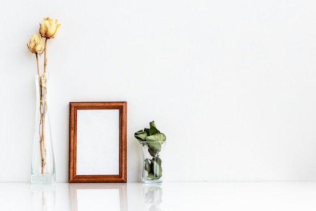 Hölzerner Fotorahmen und trockene weiße Rosen in einer Vase auf weißem Hintergrund Minimalistisches, sanftes Sommerlayout Leer für eine Postkarte Interieur für Design