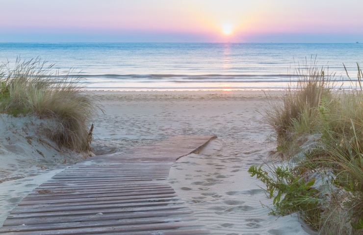 Foto hölzerner gehweg, der den strand bei sonnenaufgang betritt