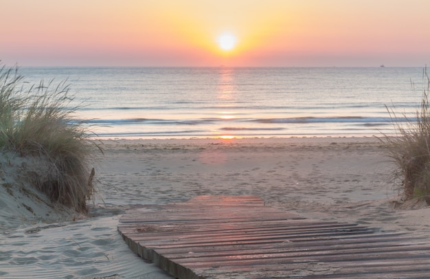 Hölzerner Gehweg, der den Strand bei Sonnenaufgang betritt