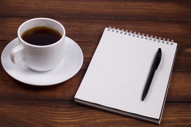 Hölzerner Hintergrund der Kaffeetasse, des Notizblockes und des Stiftes