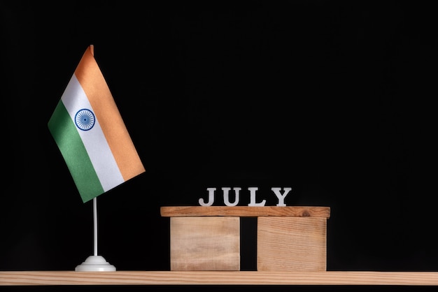 Hölzerner Juli-Kalender mit indischer Flagge auf schwarzem Hintergrund. Feiertage von Indien im Juli.