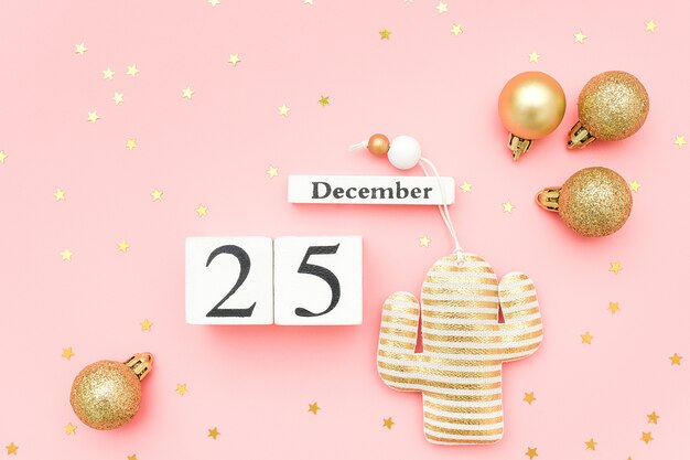 Hölzerner Kalender am 25. Dezember, Goldtextilweihnachtskaktus und Sternkonfettis auf rosa Hintergrund.