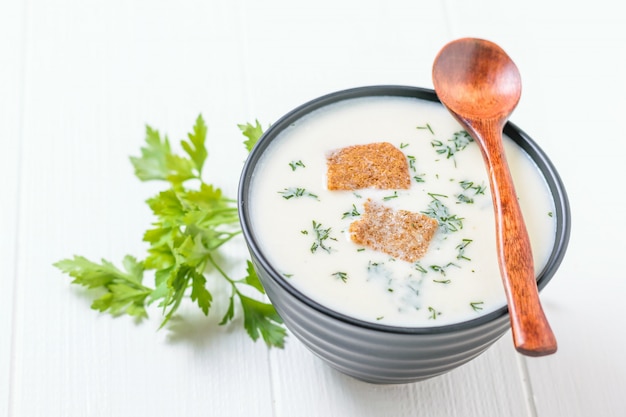 Hölzerner Löffel auf einer Blumenkohlsuppe der Schüssel mit Sahne auf einer weißen Tabelle.