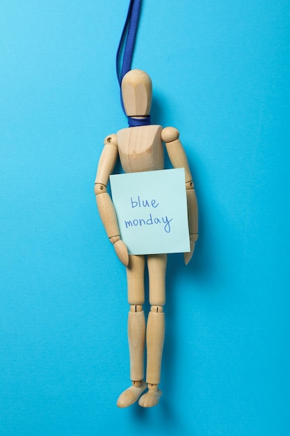 Hölzerner Mann auf blauem Band mit Papier mit dem Text Blue Monday auf blauem Hintergrund, Draufsicht