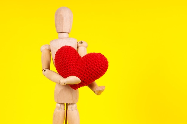 Hölzerner Mann mit einem roten Herzen in seinen Händen auf einem gelben Hintergrund Hochwertiges Foto
