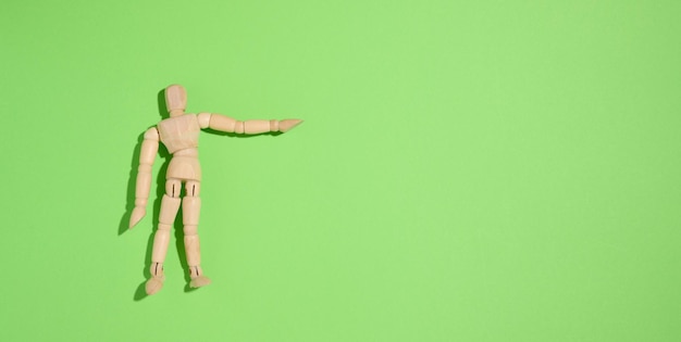Hölzerner Marionettenmann auf einem grünen Hintergrund, der mit seiner Hand zeigt