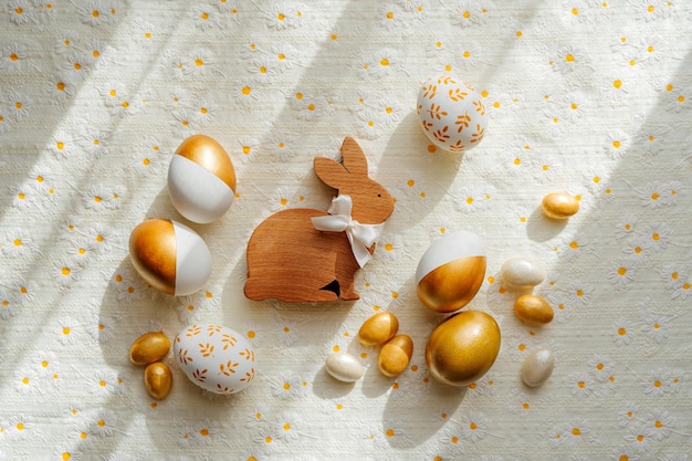 Hölzerner Osterhase und goldene Eier mit Süßigkeiten auf dem Tisch Urlaubskonzept Frohe Ostern