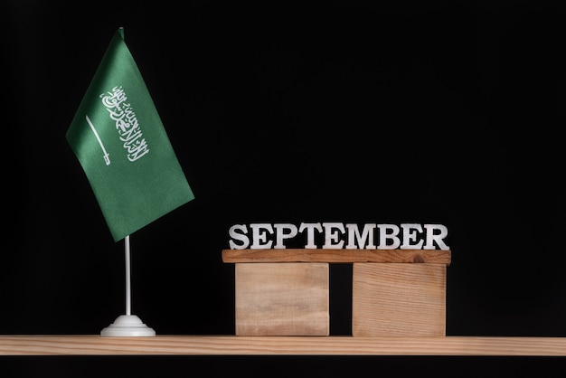 Hölzerner Septemberkalender mit Saudi-Arabien-Flagge auf Schwarzem. Termine von Saudi-Arabien im September.