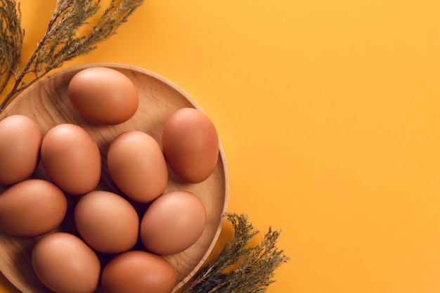 Hölzerner Teller mit Osterei-Lebensmittel und Trockenblume auf Draufsicht des gelben Hintergrundes der Weinleseart