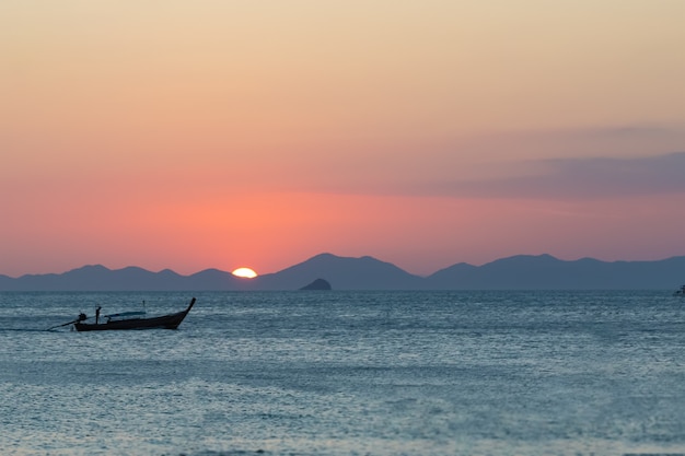 Hölzernes Fischerboot, das auf dem Meer vor dem Hintergrund des Sonnenuntergangs und der Berge segelt