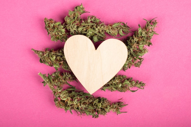 Hölzernes Herz auf Marihuana-Knospen auf rosafarbenem Hintergrund, Liebes- und Valentinsgrußsymbolkopienraum.