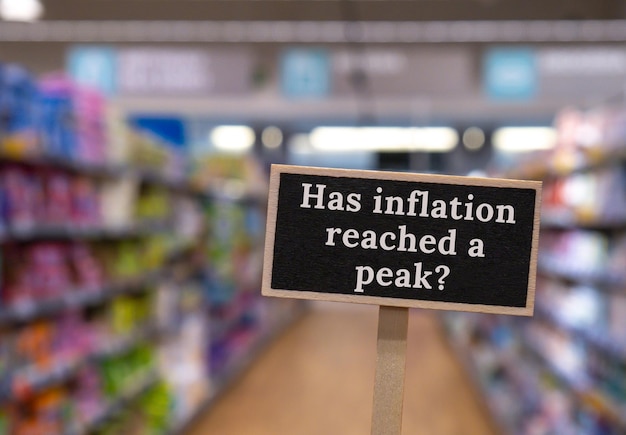 Hölzernes Hinweisschild mit Text HAT DIE INFLATION EINE SPITZE ERREICHT, gegen einen defokussierten Laden