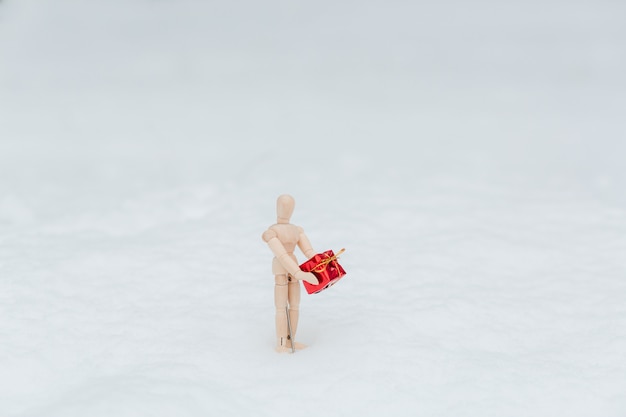 Hölzernes Mannequin mit dem Geschenk auf dem Schnee