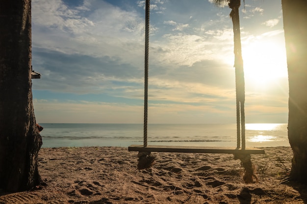 Hölzernes Schwingen, das am Strand mit Sonnenaufgang hängt.