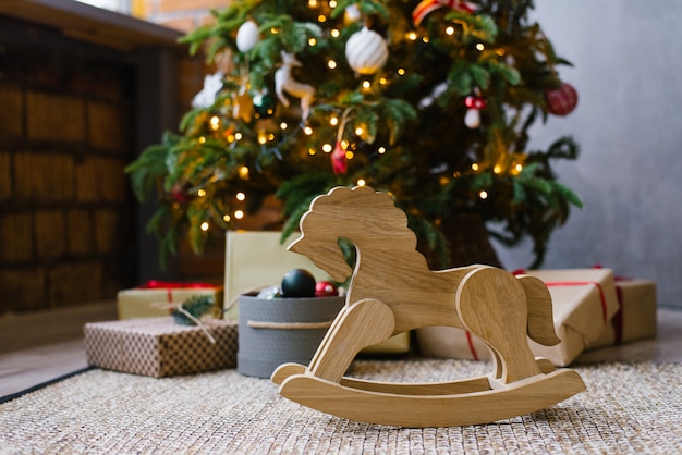 Foto hölzernes spielzeugpferd auf dem hintergrund eines weihnachtsbaums mit geschenken