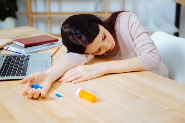 Hör auf zu schlafen. Kranke weibliche Person, die die Augen geschlossen hält und Tabletten in der rechten Hand hält, während sie sie nimmt