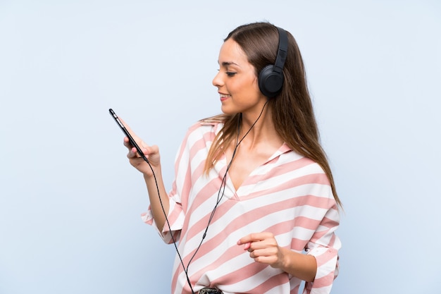 Hörende Musik der jungen Frau mit einem Mobile über blauer Wand