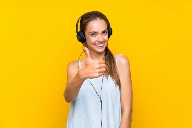 Hörende musik der jungen frau über lokalisierter gelber wand mit den daumen oben, weil etwas gutes geschehen ist