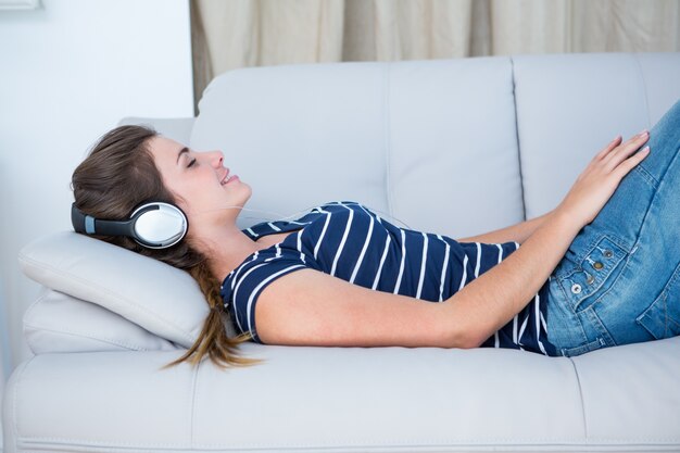 Hörende Musik des hübschen Brunette auf Couch