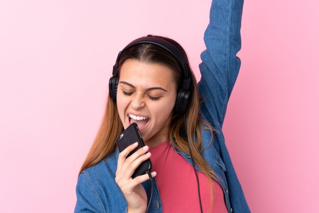 Hörende Musik des Jugendlichmädchens mit einem Mobile über lokalisierter rosa Wand