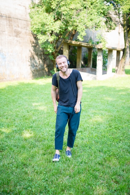 hörende Musik des modernen stilvollen blonden Mannes des Hippies im Park