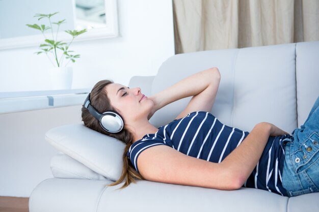Hörende Musik des ruhigen Brunette auf Couch