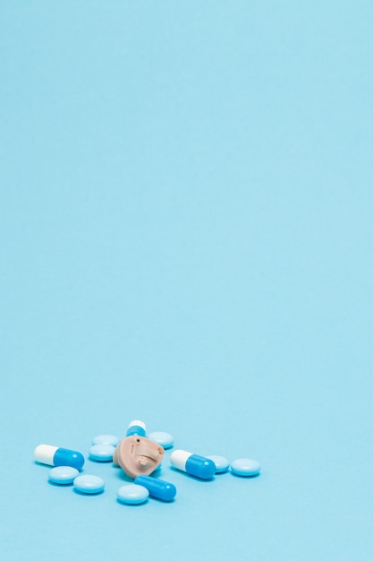 Hörgerät und blaue Pillen auf blauem Hintergrund
