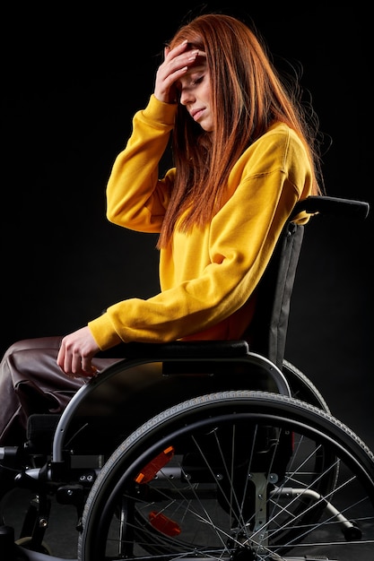 hoffnungslose Frau sitzt unglücklich im Rollstuhl, mit depressivem Gesichtsausdruck, sie leidet an Behinderung. isolierter schwarzer Hintergrund. Seitenansicht