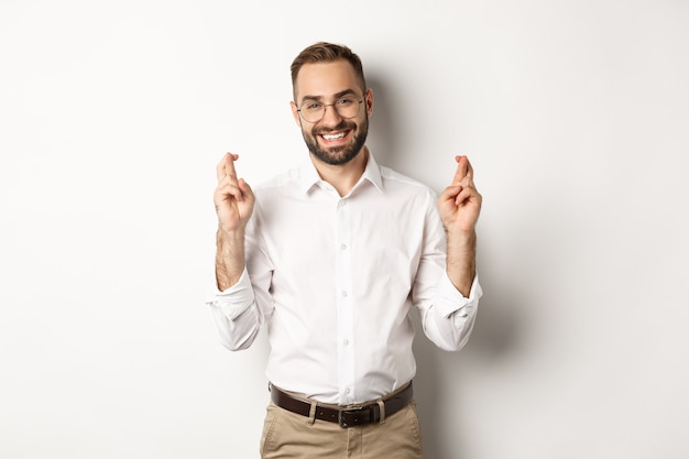 Hoffnungsvoller optimistischer Mann, der einen Wunsch macht, die Finger kreuzt und betet und auf weißem Hintergrund steht. Platz kopieren