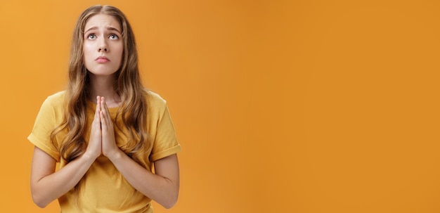 Foto hoffnungsvolles, unruhiges und besorgtes, düsteres, treues mädchen im t-shirt, das hände hält, um gegen die brust zu schauen