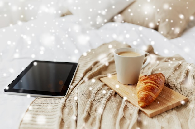 hogar acogedor, concepto de mañana e invierno - computadora tablet, taza de café y croissant en la cama sobre la nieve