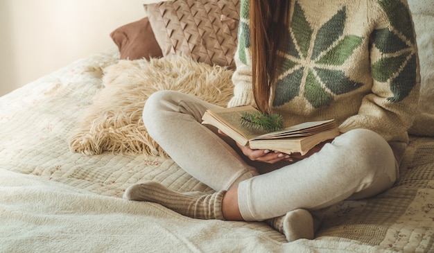 Hogar acogedor. Hermosa mujer está leyendo un libro en la cama. Buenos días con té y libro. Bastante joven relajante. El concepto de lectura