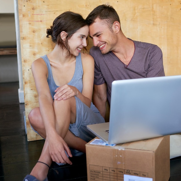 El hogar es donde comienza nuestra historia. Imagen de una joven pareja cariñosa que usa una computadora portátil en el piso de su casa.