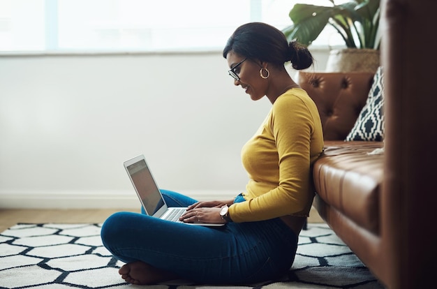 El hogar es donde me siento más cómodo Toma completa de una mujer joven y atractiva sentada sola en casa y usando su computadora portátil