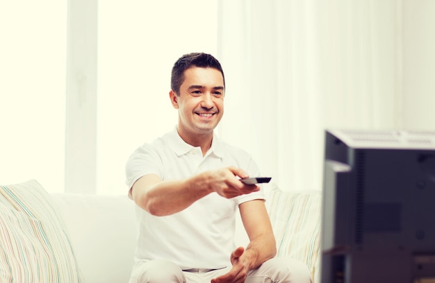 hogar, gente, tecnología y concepto de entretenimiento - hombre sonriente con control remoto viendo televisión en casa