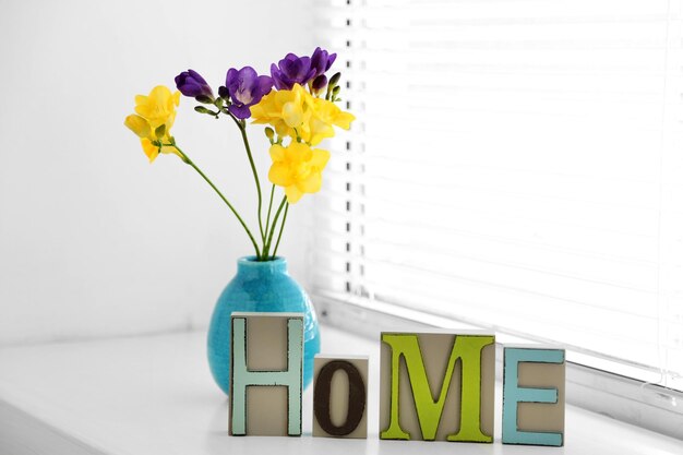 Hogar en letras coloridas y flores de primavera en un interior blanco claro