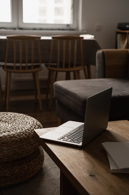 Hogar minimalista estético, diseño de interiores de sala de estar. Mesa de madera con ordenador portátil, puf de ratán, taburetes