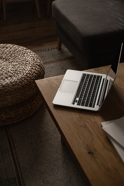 Hogar minimalista estético, diseño de interiores de sala de estar. Mesa de madera con ordenador portátil, puf de ratán, taburetes