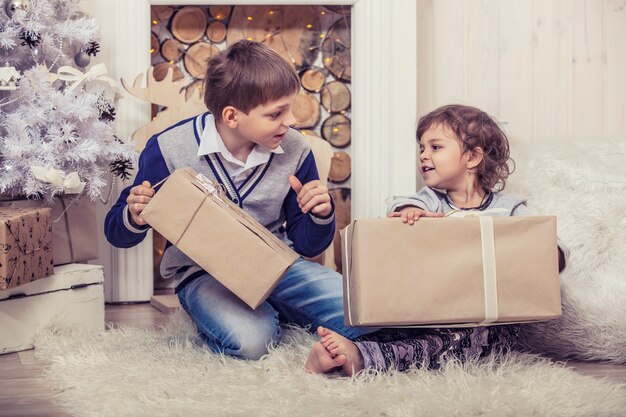 Hogar de un niño y una niña felices con cajas de regalos en el interior de Navidad