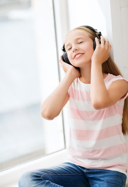 hogar, ocio, nuevas tecnologías y concepto de música - niña con auriculares en casa