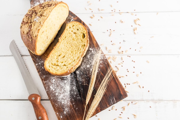 Una hogaza cortada de delicioso pan casero en una tabla y una mesa blanca de madera ven un cuchillo para cortar pan una copia del espacio