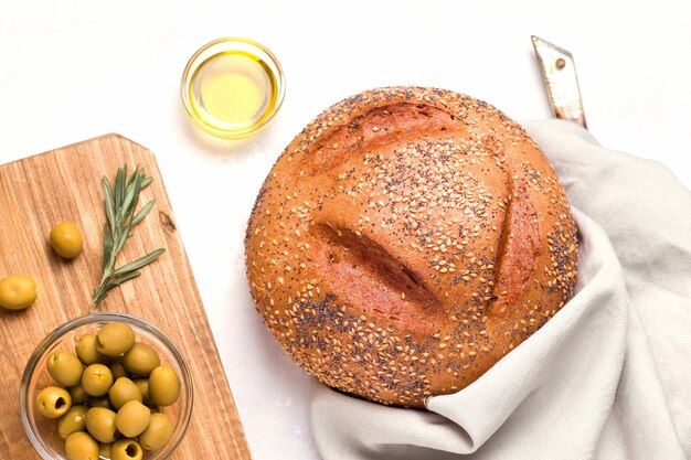 Una hogaza de pan blanco redondo en un plato blanco junto a aceitunas y mantequilla. pan casero