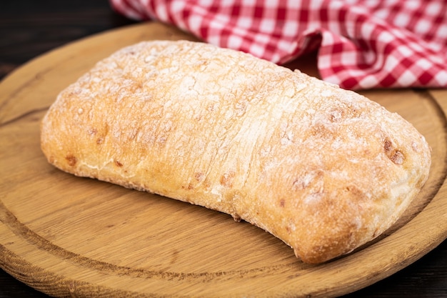 Hogaza de pan ciabatta sobre una tabla para cortar sobre la mesa de madera oscura.