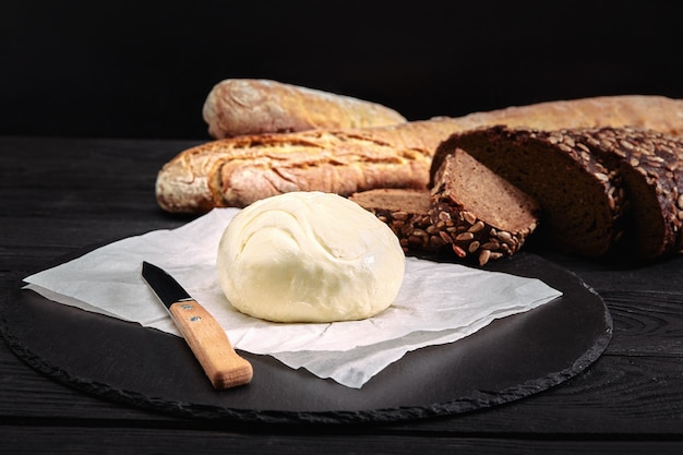 Hogaza de pan con mantequilla y cuchillo. Fondo oscuro, vista lateral.