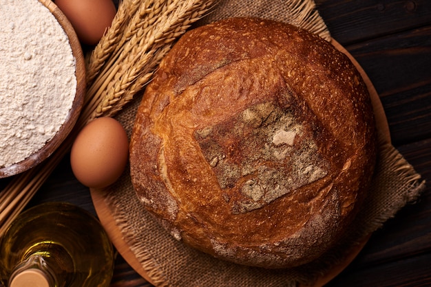 Hogaza de pan sobre una superficie de madera con harina, aceite vegetal con huevos