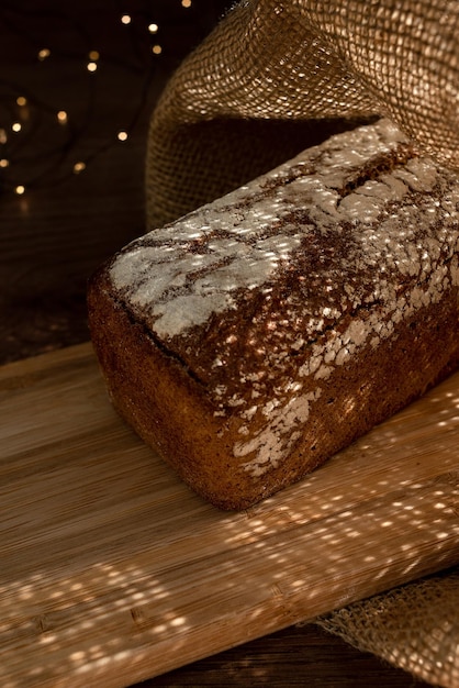 Una hogaza de pan sobre una tabla de bambú, espolvoreada con copos de avena, en una bolsa de arpillera con guirnaldas