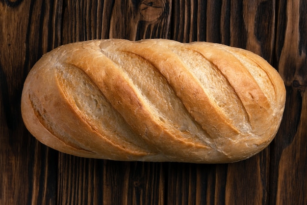 Hogaza de pan de trigo blanco acostado sobre las tablas con textura de madera oscura